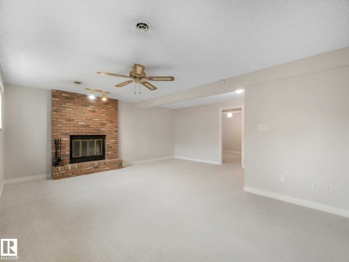 Spacious room featuring a brick fireplace with a raised hearth, light-toned carpeting, and a ceiling fan - 4011 104 Street, Edmonton, AB - Indoor With Fireplace