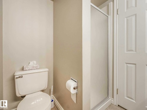 White toilet with a built-in shower stall featuring a frosted glass door and a white paneled door - 4011 104 Street, Edmonton, AB - Indoor Photo Showing Bathroom