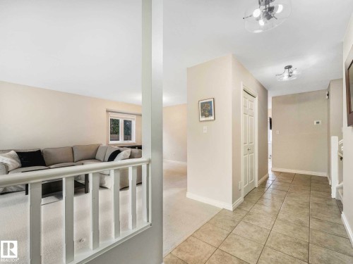 Tiled entryway with overhead lighting, leading to carpeted living areas and a traditional baluster railing - 4011 104 Street, Edmonton, AB - Indoor Photo Showing Other Room