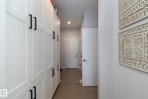 Hallway featuring extensive white built-in cabinetry with black bar pulls, recessed lighting, and wood-finish flooring - 1448 Darby Green Green, Edmonton, AB - Indoor Photo Showing Other Room