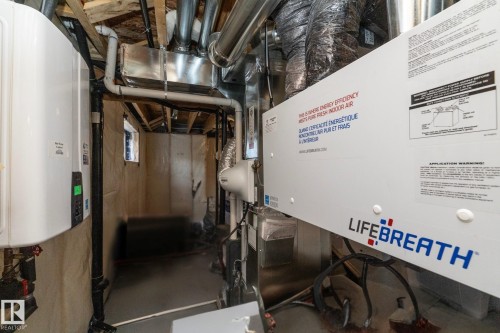 Basement utility area featuring exposed wood joists, a white tankless water heater, extensive ductwork, and a Lifebreath air purification system - 1448 Darby Green Green, Edmonton, AB - Indoor Photo Showing Basement