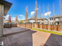 Multi-level deck with composite decking and metal railings, featuring a verdant lawn, mature trees, and a privacy fence - 