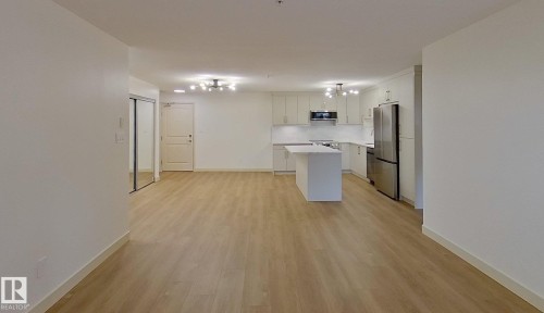 Open-concept living space featuring wood-finish flooring, a contemporary kitchen island, white cabinetry, integrated stainless steel appliances, and modern overhead lighting - 353 2096 Blackmud Creek Drive, Edmonton, AB - Indoor With Fireplace