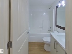 Bathroom featuring wood-finish flooring, a white vanity with an integrated sink, a dark-framed mirror, and a full bathtub with a shower - 