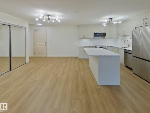 Open-concept living space featuring wood-finish flooring, a modern kitchen with light cabinetry, stainless steel appliances, a center island with a white countertop, and contemporary ceiling light fixtures - 353 2096 Blackmud Creek Drive, Edmonton, AB - Indoor Photo Showing Other Room