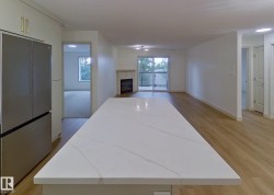 Kitchen island with a white veined countertop, stainless steel refrigerator, and light wood-finish flooring - 