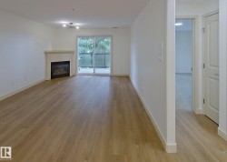 Spacious living area featuring wood-finish flooring, a white mantel fireplace, and a sliding glass door opening to a private balcony with glass railing - 