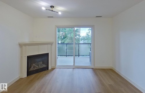 Spacious interior featuring wood-finish flooring, a built-in fireplace with a decorative mantel, and a sliding glass door opening to a private balcony - 353 2096 Blackmud Creek Drive, Edmonton, AB - Indoor Photo Showing Other Room With Fireplace