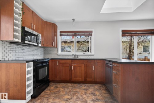 Kitchen featuring wood cabinetry, stainless steel microwave, black electric range, white subway tile backsplash, and dark countertops - 10409 83 Street, Edmonton, AB - Indoor Photo Showing Kitchen