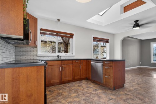 Kitchen featuring wood cabinetry, dark countertops, a subway tile backsplash, and stainless steel appliances - 10409 83 Street, Edmonton, AB - Indoor Photo Showing Kitchen