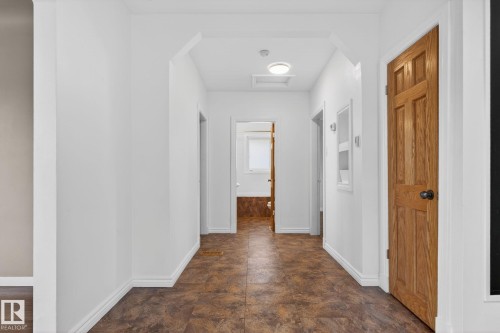 Hallway featuring wood-finish flooring, white walls, white baseboards, and a wood-panel door with a black knob - 10409 83 Street, Edmonton, AB - Indoor Photo Showing Other Room