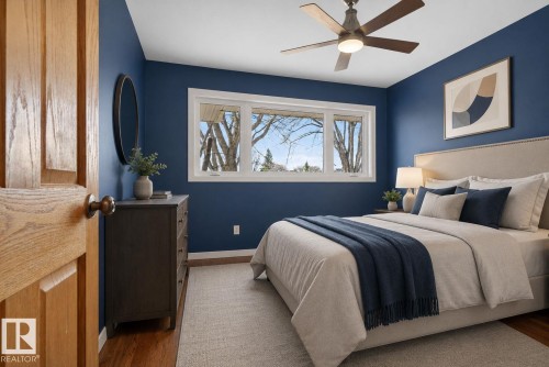 Bedroom featuring rich blue walls, wood-finish flooring, a multi-pane window, and a ceiling fan with integrated lighting - 10409 83 Street, Edmonton, AB - Indoor Photo Showing Bedroom