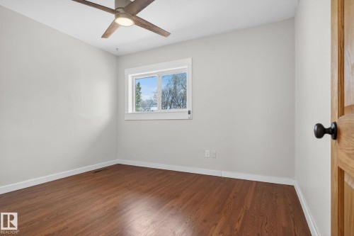 Spacious room featuring wood-finish flooring, a contemporary ceiling fan with integrated lighting, a large window providing natural illumination, and crisp white trim - 10409 83 Street, Edmonton, AB - Indoor Photo Showing Other Room