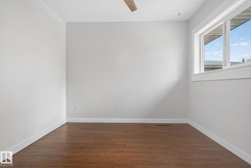 Bright room featuring wood-finish flooring, white baseboards, a large window with white trim, and a ceiling fan - 10409 83 Street, Edmonton, AB - Indoor Photo Showing Other Room
