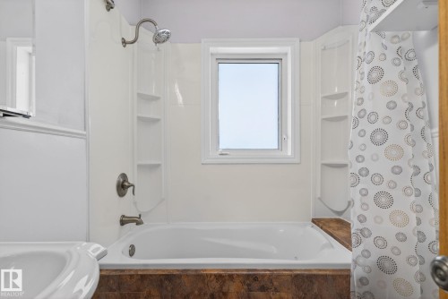 White soaking tub with integrated shower, accented by bronze-finish fixtures - 10409 83 Street, Edmonton, AB - Indoor Photo Showing Bathroom