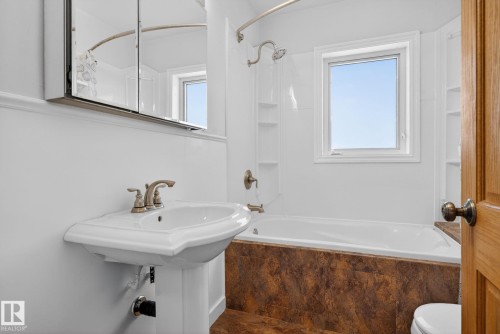 Pedestal sink with bronze-finish faucet, framed mirror medicine cabinet, built-in bathtub with shower, integrated shelving, and a window providing natural light - 10409 83 Street, Edmonton, AB - Indoor Photo Showing Bathroom
