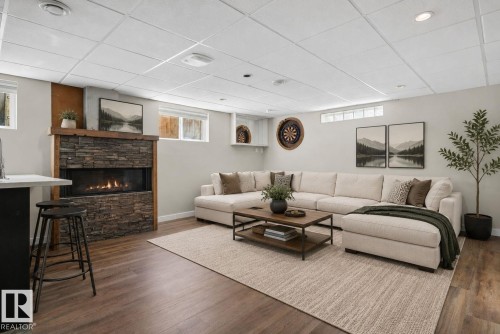 Spacious living area featuring a stone-clad fireplace with a natural wood mantel, wood-finish flooring, and recessed lighting - 10409 83 Street, Edmonton, AB - Indoor Photo Showing Living Room With Fireplace