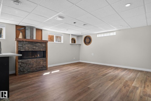 Spacious room featuring wood-finish flooring, a stone-front fireplace with a wood mantle, and recessed lighting - 10409 83 Street, Edmonton, AB - Indoor Photo Showing Other Room