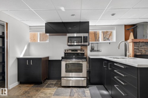 Kitchenette featuring stainless steel appliances, dark wood-finish cabinetry with silver hardware, light-toned countertops, and a stainless steel sink with a gooseneck faucet - 10409 83 Street, Edmonton, AB - Indoor Photo Showing Kitchen