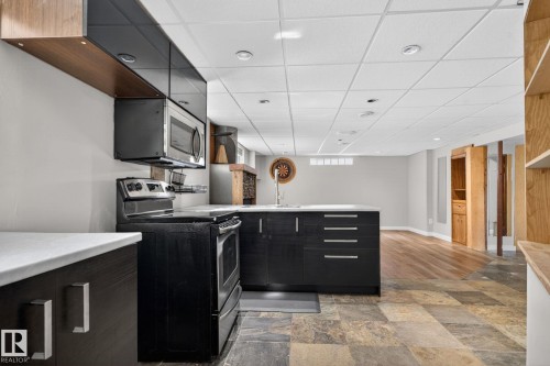 Compact kitchen featuring black cabinetry with silver hardware, an integrated microwave, and a black electric range - 10409 83 Street, Edmonton, AB - Indoor Photo Showing Kitchen