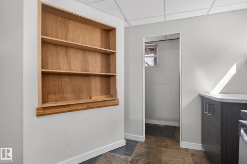 Built-in wood shelving unit, slate-style flooring, white walls, drop ceiling, and dark wood-finish cabinetry with a light countertop - 10409 83 Street, Edmonton, AB - Indoor Photo Showing Other Room