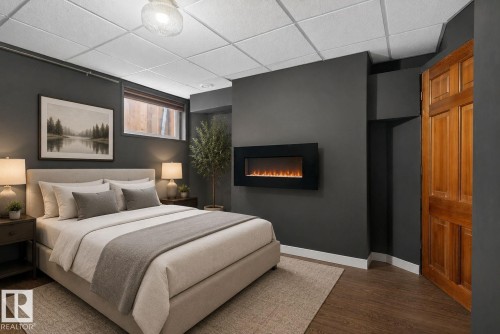 Bedroom featuring a wall-mounted electric fireplace, wood-finish flooring, dark wall paint, and a wood panel door - 10409 83 Street, Edmonton, AB - Indoor Photo Showing Bedroom