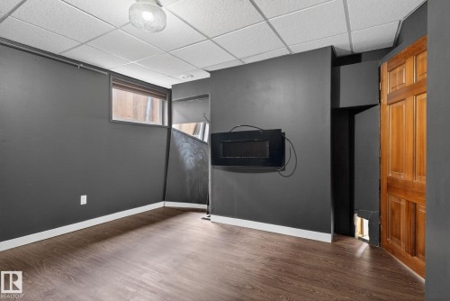 Room featuring dark-toned walls, wood-finish flooring, a suspended ceiling, and a single window - 10409 83 Street, Edmonton, AB - Indoor Photo Showing Other Room