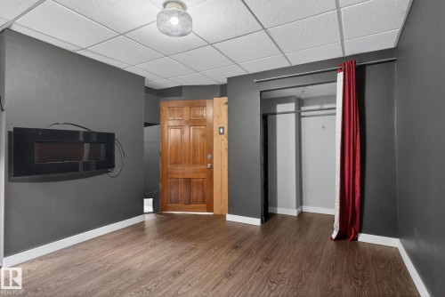 Room featuring wood-finish flooring, a wall-mounted electric fireplace, and a drop ceiling - 10409 83 Street, Edmonton, AB - Indoor Photo Showing Other Room