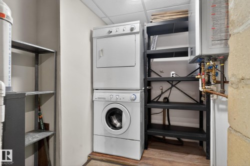 Dedicated utility area featuring a stacked washer and dryer, adjacent shelving, and a wall-mounted water heater - 10409 83 Street, Edmonton, AB - Indoor Photo Showing Laundry Room