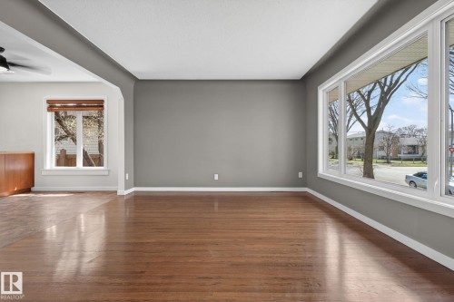 Bright interior space featuring wood-finish flooring, a large multi-pane window, neutral gray wall tones, white trim, and an architectural archway - 10409 83 Street, Edmonton, AB - Indoor Photo Showing Other Room