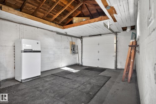 Single-car garage featuring a roll-up door, exposed wood beam ceiling, concrete flooring, and a window for natural light - 10409 83 Street, Edmonton, AB - Indoor Photo Showing Garage