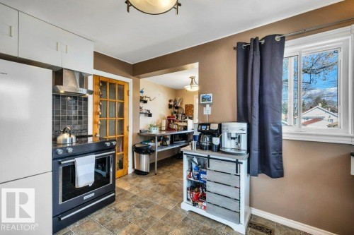 Functional kitchen featuring a stainless steel range hood, dark square tile backsplash, and a light wood-finish door with glass panels - 11445 68 Street, Edmonton, AB - Indoor Photo Showing Kitchen