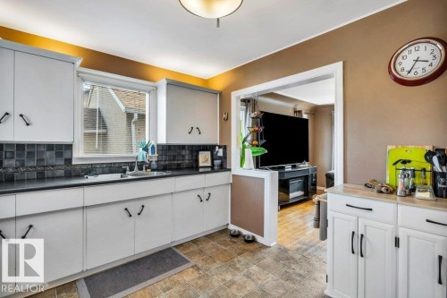 Galley kitchen featuring light-toned cabinetry with black hardware, dark countertops, and a dark square tile backsplash - 11445 68 Street, Edmonton, AB - Indoor Photo Showing Kitchen With Double Sink