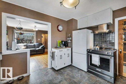 Kitchen featuring tile flooring, white upper cabinetry, stainless steel range with overhead vent, and a white refrigerator - 11445 68 Street, Edmonton, AB - Indoor Photo Showing Kitchen