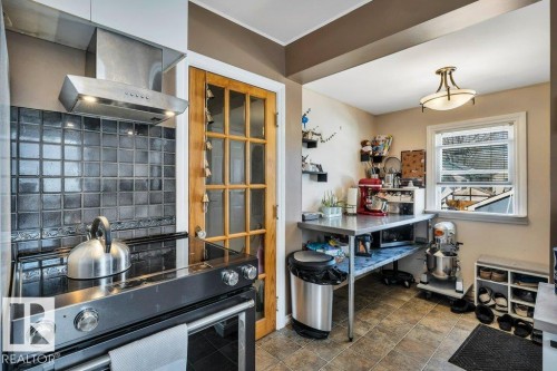 Kitchen area featuring a stainless steel range hood, black tile backsplash, and a paneled wood door - 11445 68 Street, Edmonton, AB - Indoor Photo Showing Kitchen