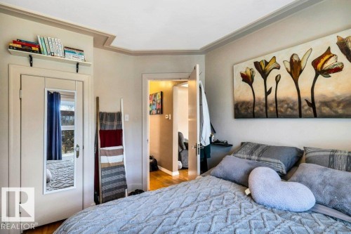 Interior room featuring crown molding, a built-in wall shelf, a door with an attached full-length mirror, and wood-finish flooring - 11445 68 Street, Edmonton, AB - Indoor Photo Showing Bedroom