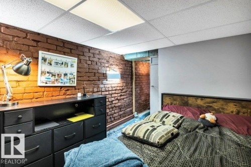 Exposed brick accent wall with a drop ceiling featuring recessed lighting panels and a painted wall surface - 11445 68 Street, Edmonton, AB - Indoor