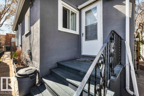 Exterior entry featuring a dark gray painted stucco finish, white-framed windows, a white storm door, and a black wrought iron handrail - 11445 68 Street, Edmonton, AB - Outdoor With Exterior