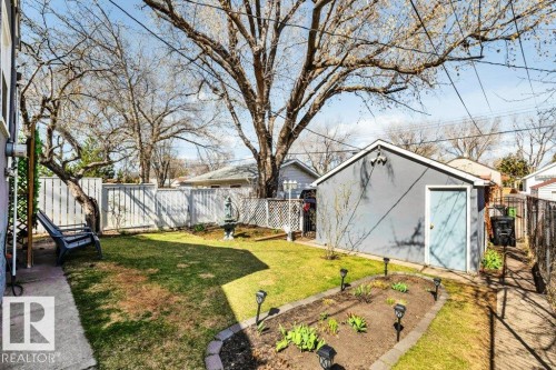 Expansive backyard featuring a detached accessory structure, mature trees, a manicured lawn, a garden bed with decorative edging and pathway lighting, and perimeter fencing - 11445 68 Street, Edmonton, AB - Outdoor