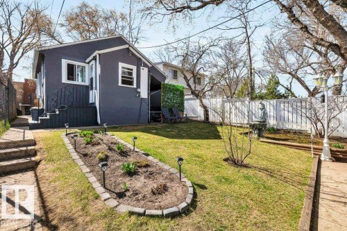 Manicured backyard featuring a stone-lined garden bed with solar path lights, a white privacy fence, and mature trees providing natural shade - 11445 68 Street, Edmonton, AB - Outdoor