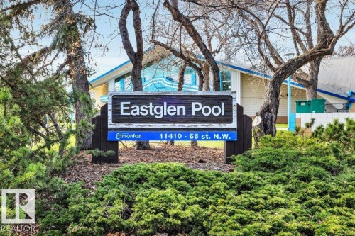 Community sign for Eastglen Pool, featuring a building with blue trim, surrounded by mature trees and manicured shrubbery - 11445 68 Street, Edmonton, AB - Outdoor
