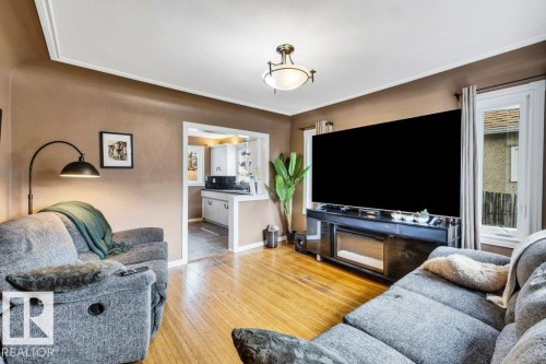 Hardwood flooring extends throughout this living area, featuring a decorative ceiling light fixture and crown molding - 11445 68 Street, Edmonton, AB - Indoor Photo Showing Living Room