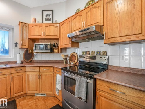 The kitchen features warm wood cabinetry, a built-in microwave, and a stainless steel oven with a range hood - 308 Beringer Crescent, Edmonton, AB - Indoor Photo Showing Kitchen