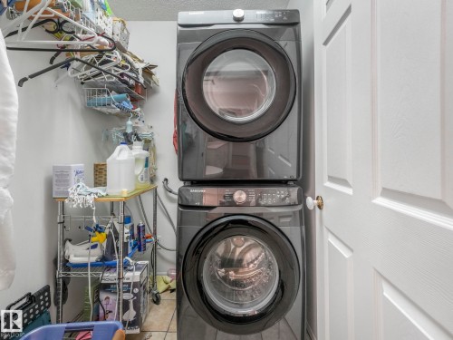 The laundry area features a stacked washer and dryer unit, white walls, and a white door with a brass doorknob - 308 Beringer Crescent, Edmonton, AB - Indoor Photo Showing Laundry Room