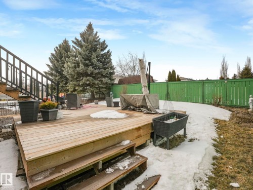 The property features an extensive outdoor deck with stairs, a green fence, and large evergreen trees - 308 Beringer Crescent, Edmonton, AB - Outdoor