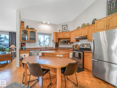 The kitchen features wood cabinetry, stainless steel appliances, and a central island with an integrated table - 308 Beringer Crescent, Edmonton, AB - Indoor Photo Showing Kitchen