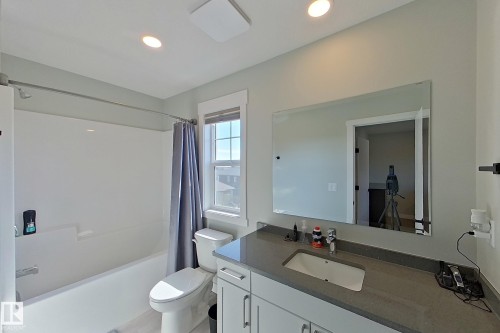 Bathroom featuring a single vanity with an integrated sink, a rectangular mirror, and a full-size bathtub with a shower - 33 150 Everitt Dr, St. Albert, AB - Indoor Photo Showing Bathroom