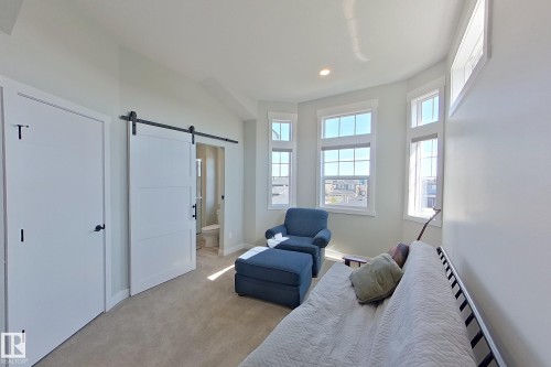 Recessed lighting illuminates a carpeted room featuring a modern barn door entry to a bathroom - 33 150 Everitt Dr, St. Albert, AB - Indoor Photo Showing Bedroom
