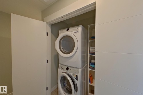 Dedicated laundry closet featuring a stacked washer and dryer, integrated shelving, white shaker-style doors, and light-toned wall paint - 33 150 Everitt Dr, St. Albert, AB - Indoor Photo Showing Laundry Room
