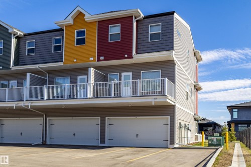 Multi-level townhome exterior featuring individual garages, private balconies with white railings, and a varied facade of horizontal siding and shingle accents in multiple colors - 33 150 Everitt Dr, St. Albert, AB - Outdoor With Exterior